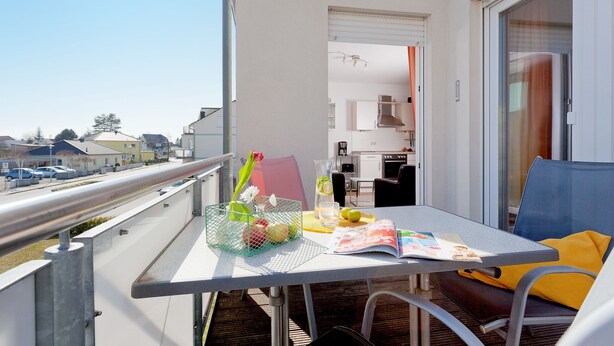 A balcony with a table set for two, a chair, a magazine, and a basket with flowers and fruits. - 2.3 - Glienbergweg 26 a Zinnowitz (Zinnowitz)
