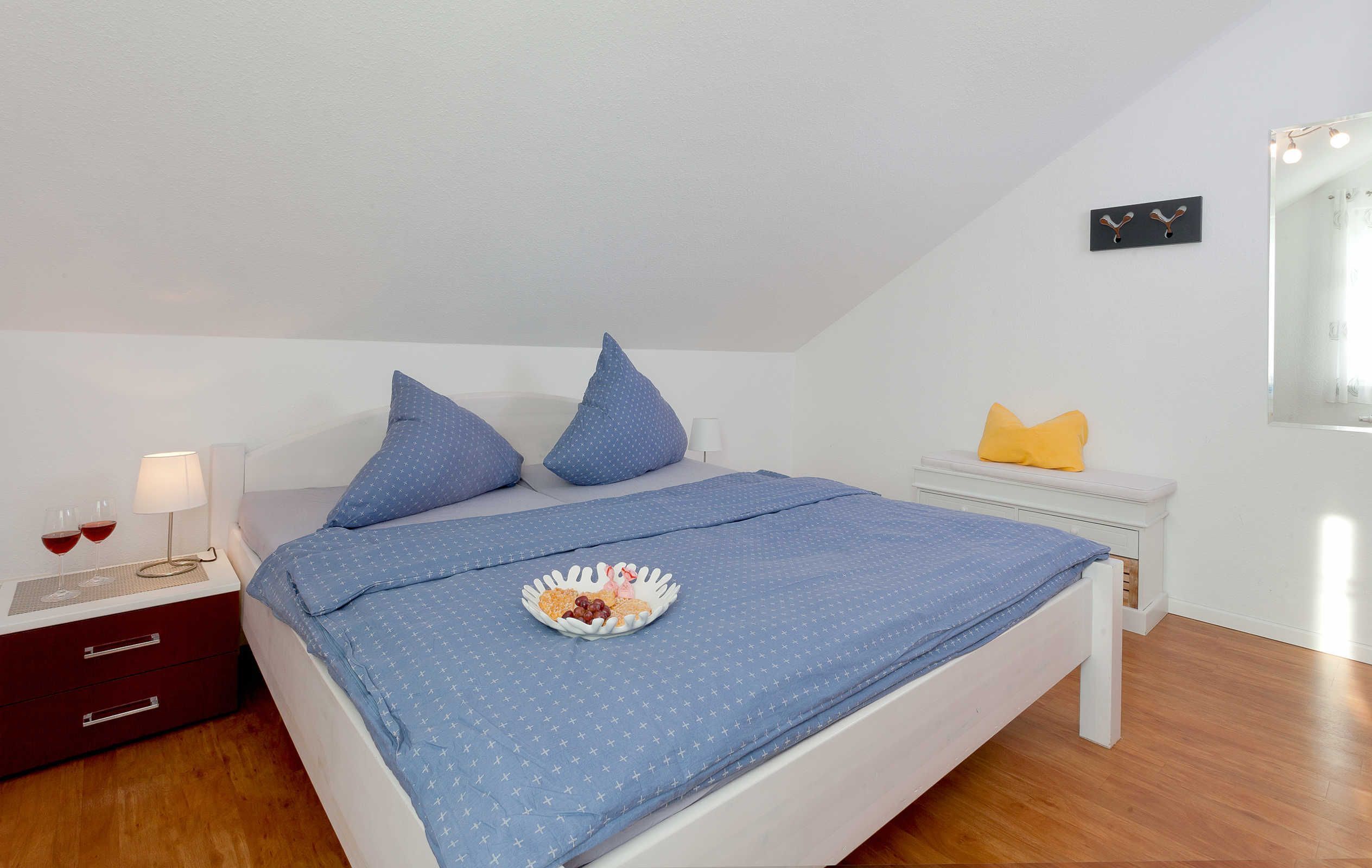 A neatly made bed with blue bedding, a bedside table with a lamp, and a small plate of food on the bed.