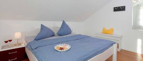 A neatly made bed with blue bedding, a bedside table with a lamp, and a small plate of food on the bed.