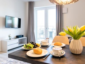 Une chambre d’hôtel avec une table à manger dressée pour le petit-déjeuner, un téléviseur à écran plat fixé au mur et une vue sur l’extérieur par la fenêtre.