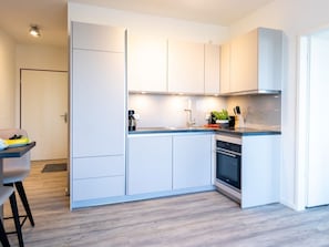 A modern kitchen with white cabinetry, a built-in oven, and a countertop with a coffee maker and a plant.
