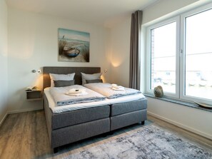 A modern bedroom with a large bed, a nightstand, a painting, and a window with curtains.
