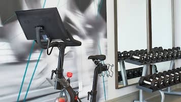 A stationary bike with a digital display, a mirror, and a rack of dumbbells in a gym.