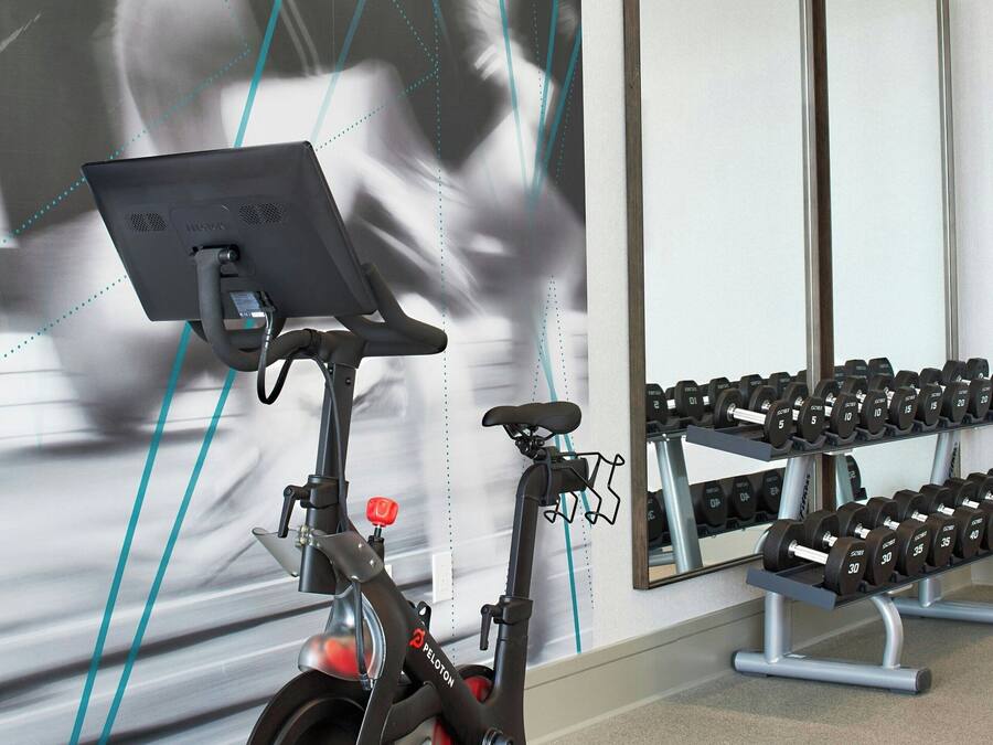 A stationary bike with a digital display, a mirror, and a rack of dumbbells in a gym.