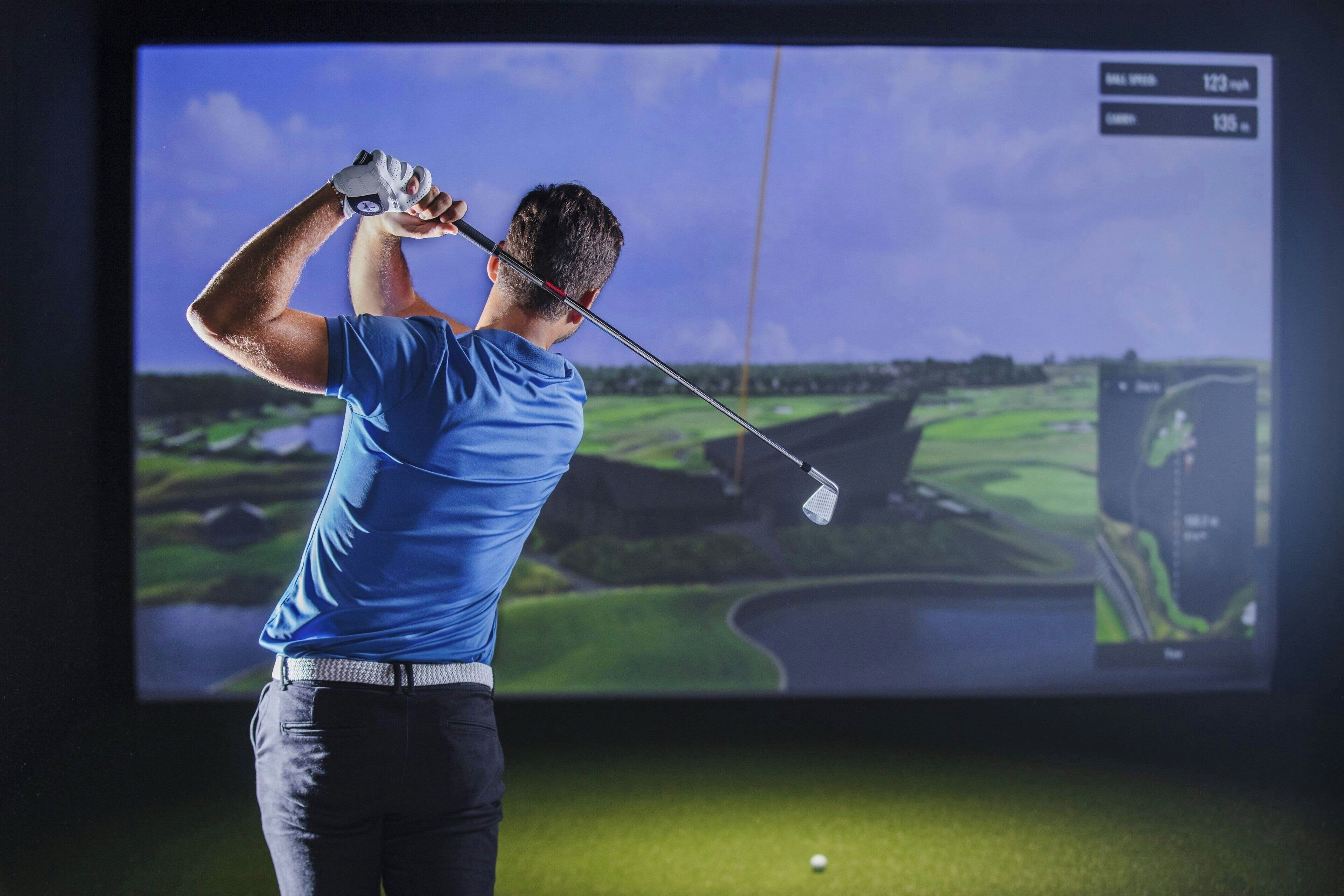 A golfer in a blue shirt and white pants swinging a golf club.