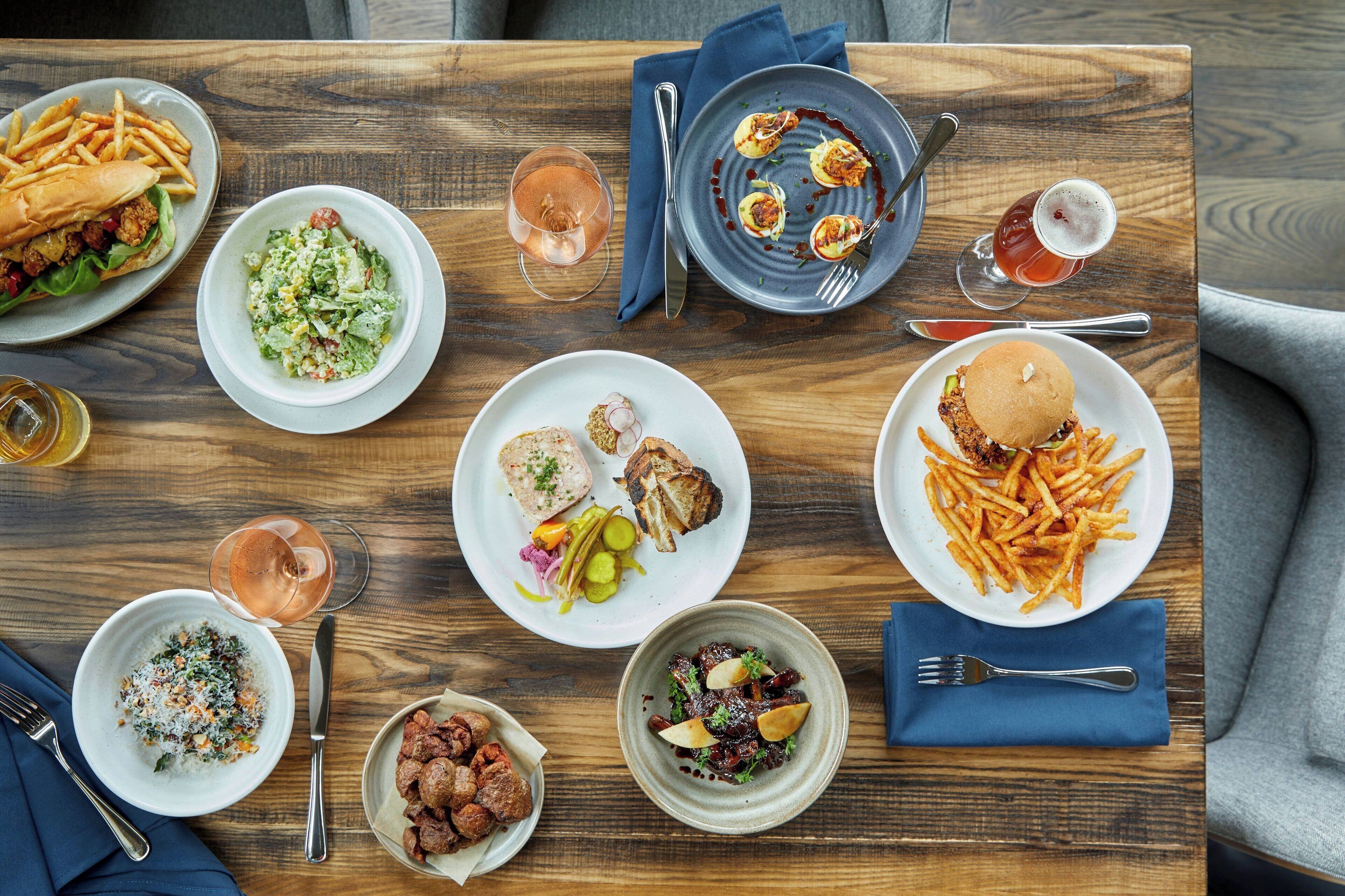 A wooden table with various dishes, including burgers, fries, salads, and appetizers.