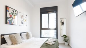 Un dormitorio moderno con una cama grande, una ventana, un televisor de pared y una planta en maceta.