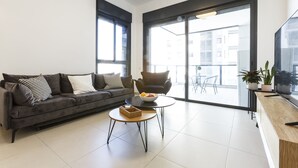 Una sala de estar moderna con un sofá, una mesa de centro, un televisor y un balcón con vistas a la ciudad.