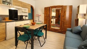 A compact living space with a kitchenette, a dining area with a table and chairs, a sofa, and a wardrobe.