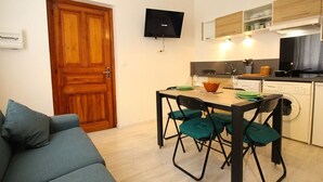 A compact living space with a wooden door, a television mounted on the wall, a dining table with chairs, and a washing machine.