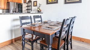 A dining table set with chairs, a kitchen area with wooden cabinets, and framed artwork on the wall.