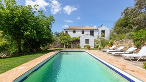 Piscina retangular com borda azulejada, rodeada por um deck de pedra.
