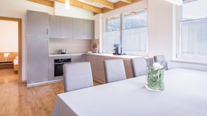A modern kitchen with wooden beams, a dining area with a table and chairs, and a view of the outdoors through large windows. - Kronsun Glück Apartment 100 m² at Kronplatz Valley Station with 3 Separate Bedrooms (Percha)