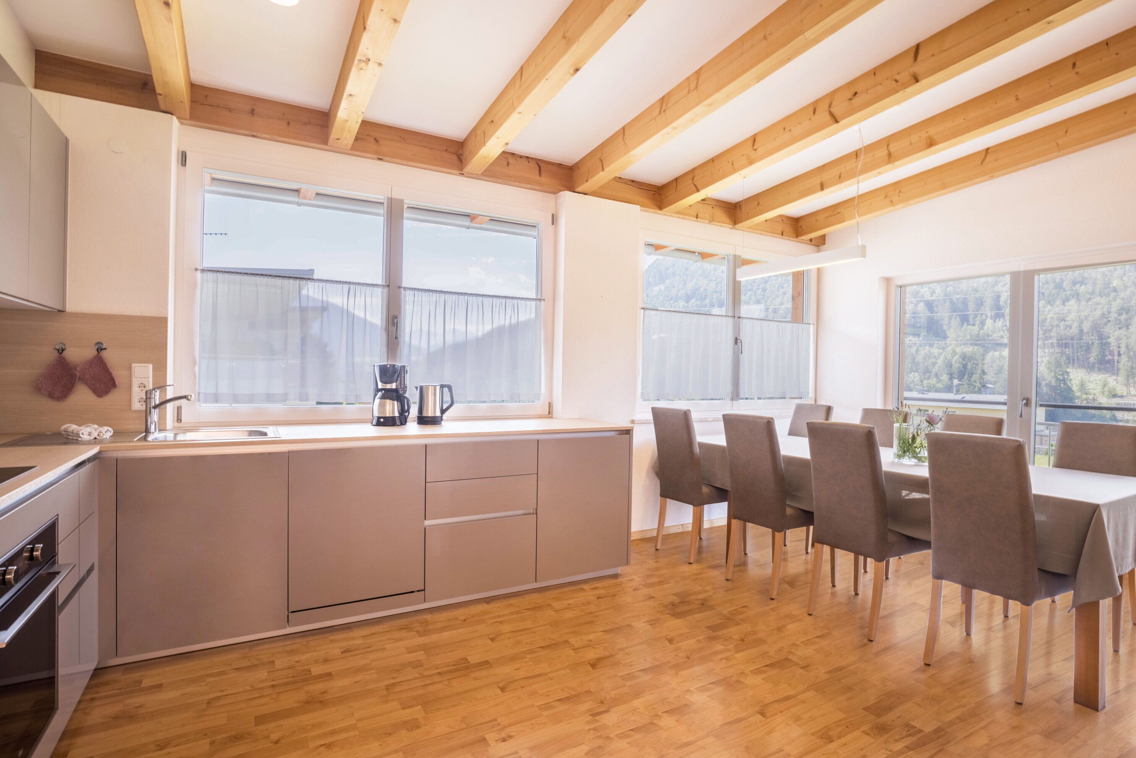 A modern kitchen with wooden beams, a dining area with chairs, and large windows.