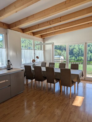 Een eetruimte met een houten plafond, grote ramen en uitzicht op een bos.