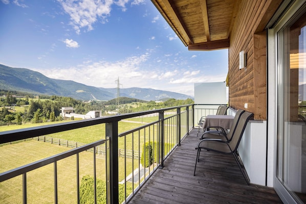 Un balcon offrant une vue sur un paysage montagneux, une terrasse en bois et des meubles d’extérieur.