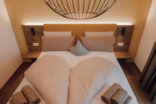 A hotel room with a large bed, two bedside tables, a wall-mounted light fixture, and a wooden headboard.