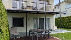 A two-story building with a balcony, a dining area with a table and chairs, and a small garden area. - Apartment Kronsun "Joy" – Directly at the Kronplatz Valley Station (Percha)