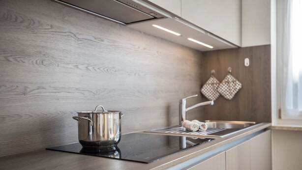 A modern kitchen with a wooden backsplash, stainless steel appliances, and a window providing natural light. - Apartment Kronsun "Joy" – Directly at the Kronplatz Valley Station (Percha)