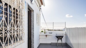A balcony with a grill, a window with decorative metalwork, and a view of the cityscape.