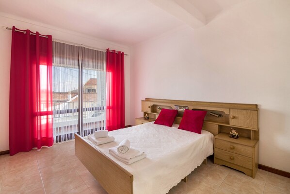 A bedroom with a bed, a nightstand, a dresser, and a window with curtains.
