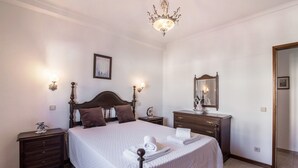 A bedroom with a bed, nightstands, a dresser, a mirror, and a chandelier.