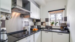 A modern kitchen with white cabinets, a black countertop, a built-in oven, and a window with a view. - Luminous Apartment Oura Nascente close to the Sea with Balcony & Wi-Fi (Albufeira)
