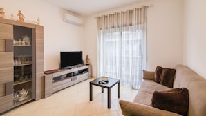 A living room with a sofa, TV, entertainment unit, and a window with curtains. - Luminous Apartment Oura Nascente close to the Sea with Balcony & Wi-Fi (Albufeira)