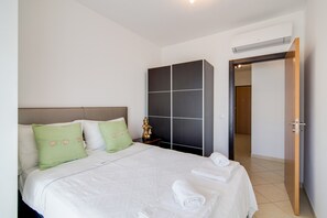 A neatly made bed with pillows, a wardrobe, and a door leading to another room. - Luminous Apartment Oura Nascente close to the Sea with Balcony & Wi-Fi (Albufeira)
