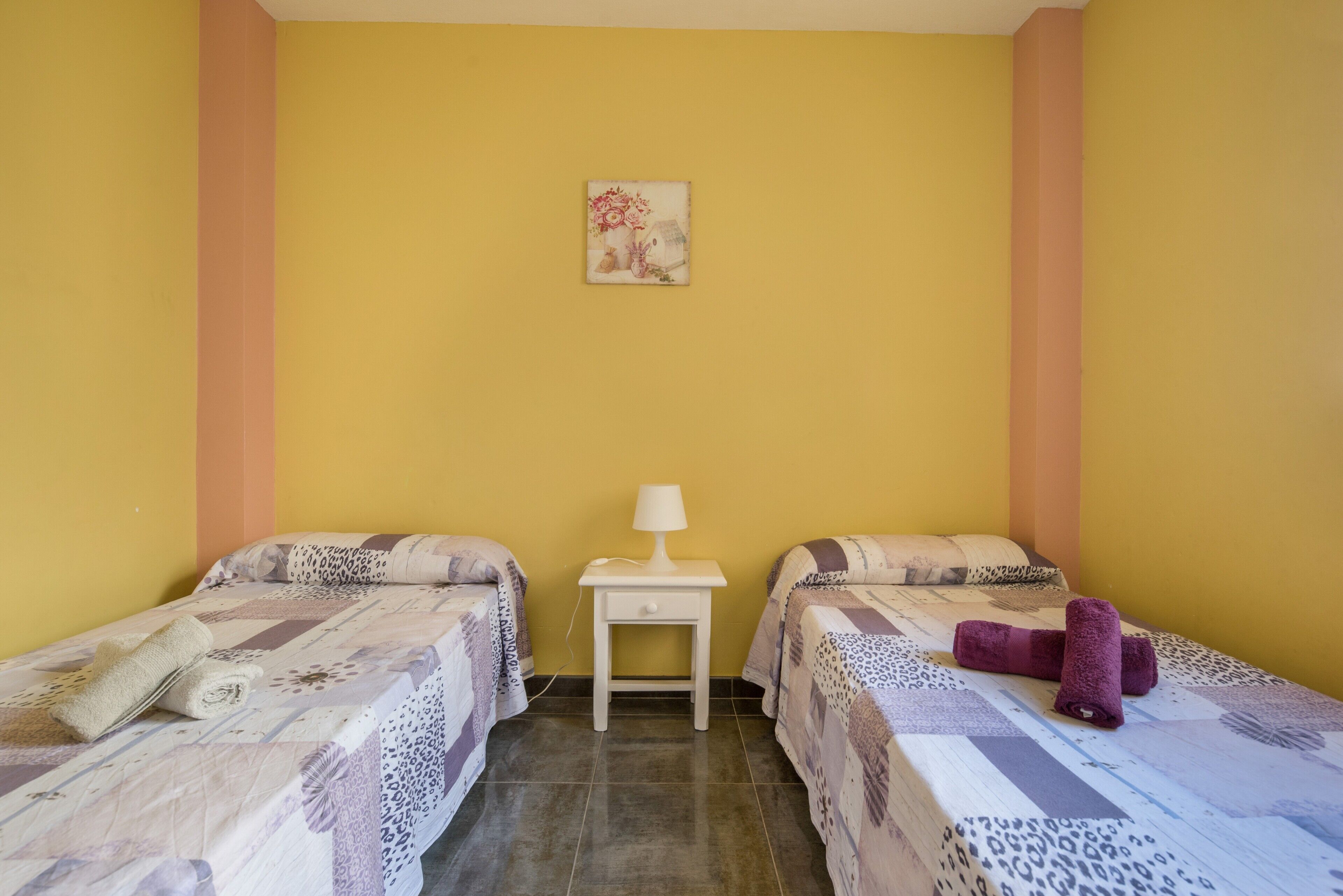 Una stanza con due letti, un comodino con una lampada e un piccolo decoro a parete.
