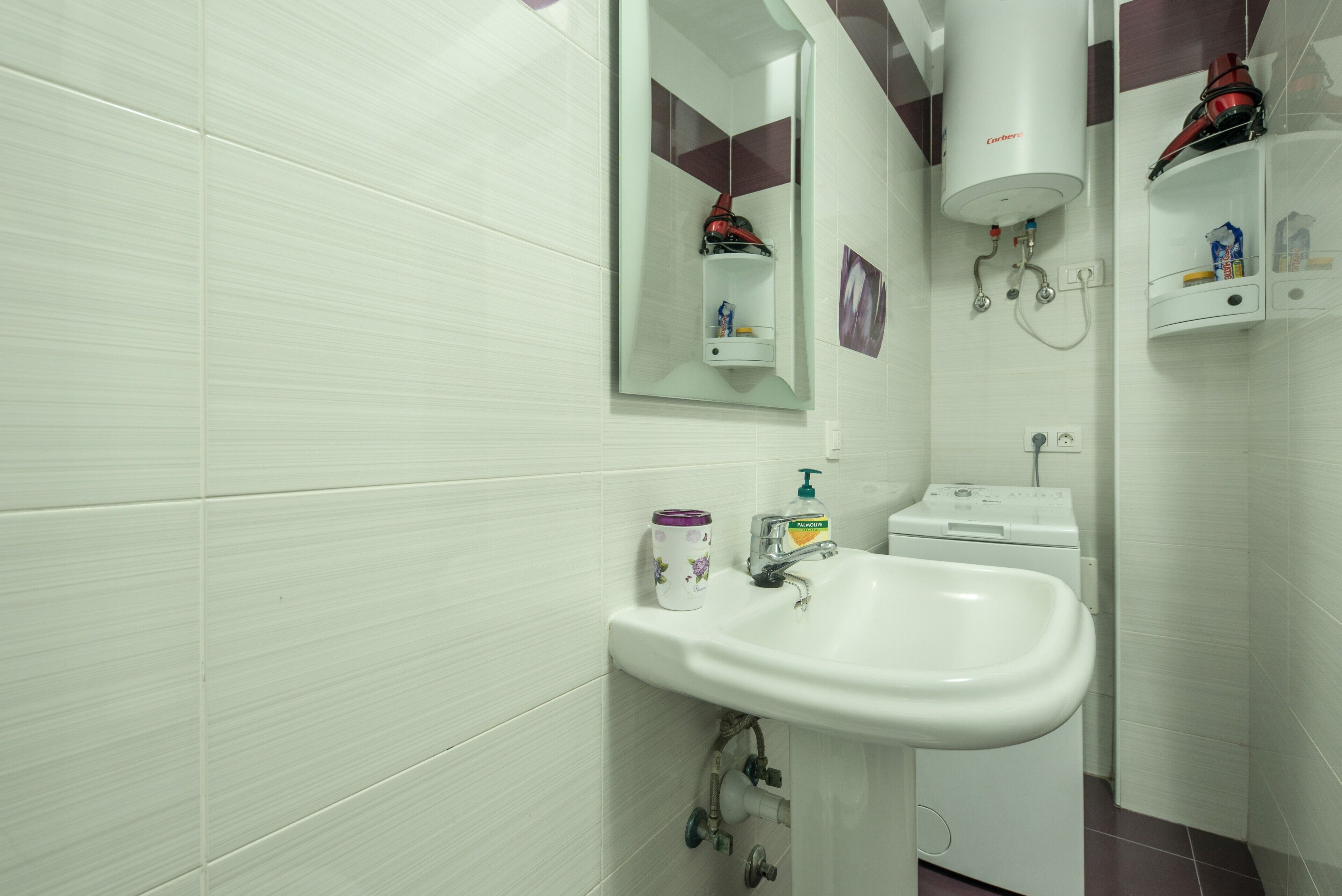 Une salle de bain avec un lavabo blanc, un miroir, un porte-serviettes, un radiateur et une étagère contenant des articles de toilette.