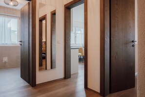 Un couloir avec un plancher en bois, une porte et une fenêtre avec des rideaux.