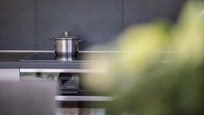 A modern kitchen with a stainless steel pot on a stove, a built-in oven, and a sleek backsplash. - Apartment 'Kronsun Harmonie' right at the Kronplatz valley station (Percha)