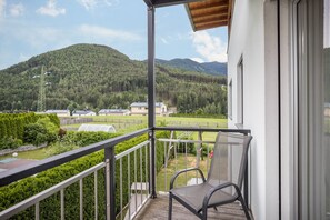 Un balcon avec une chaise, donnant sur un paysage verdoyant avec des arbres et une colline.