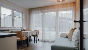 A modern living room with a sofa, dining table, chairs, and a kitchen area. - Apartment 'Kronsun Harmonie' right at the Kronplatz valley station (Percha)