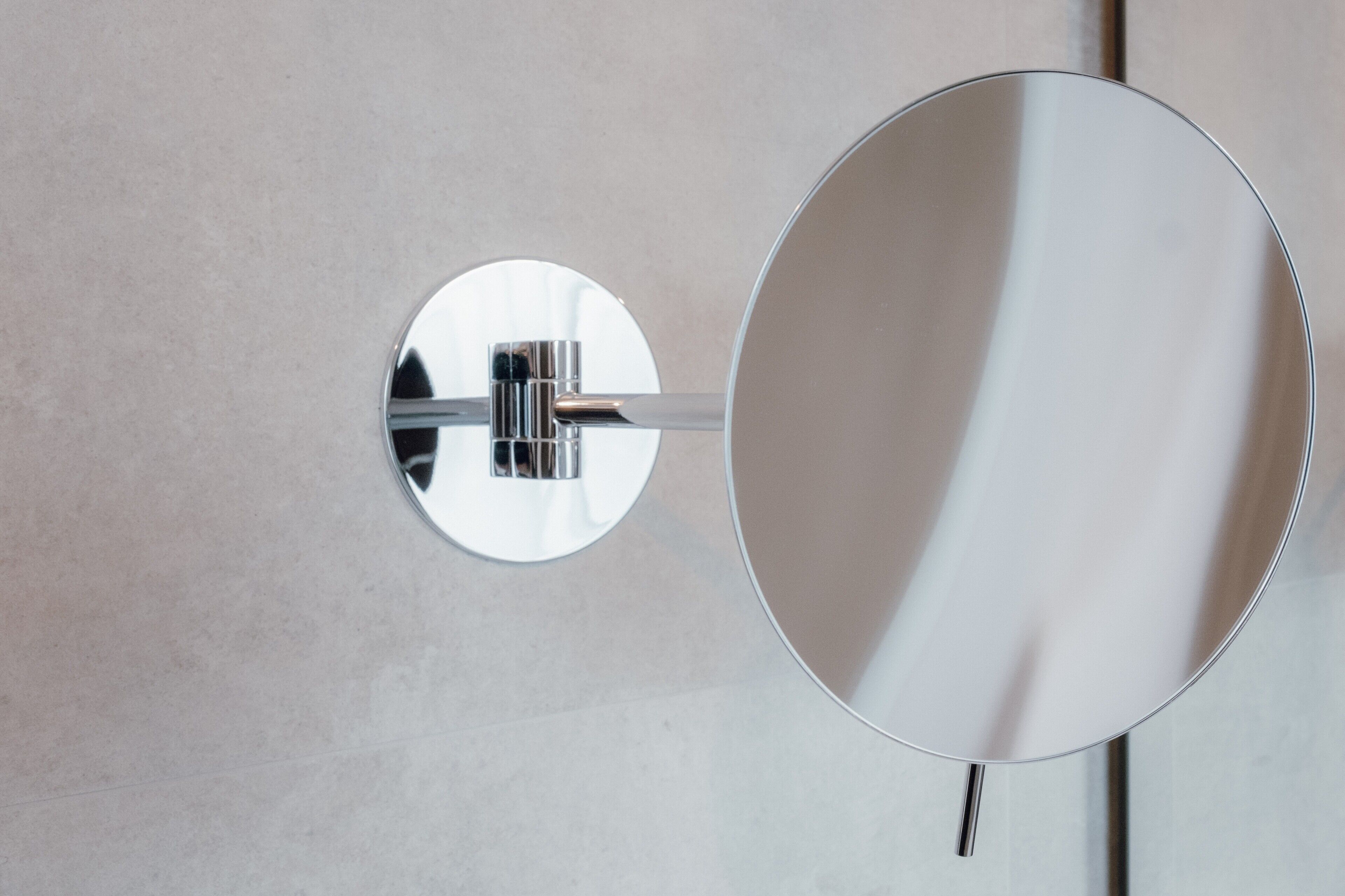 A wall-mounted mirror with a chrome fixture and a circular mirror.