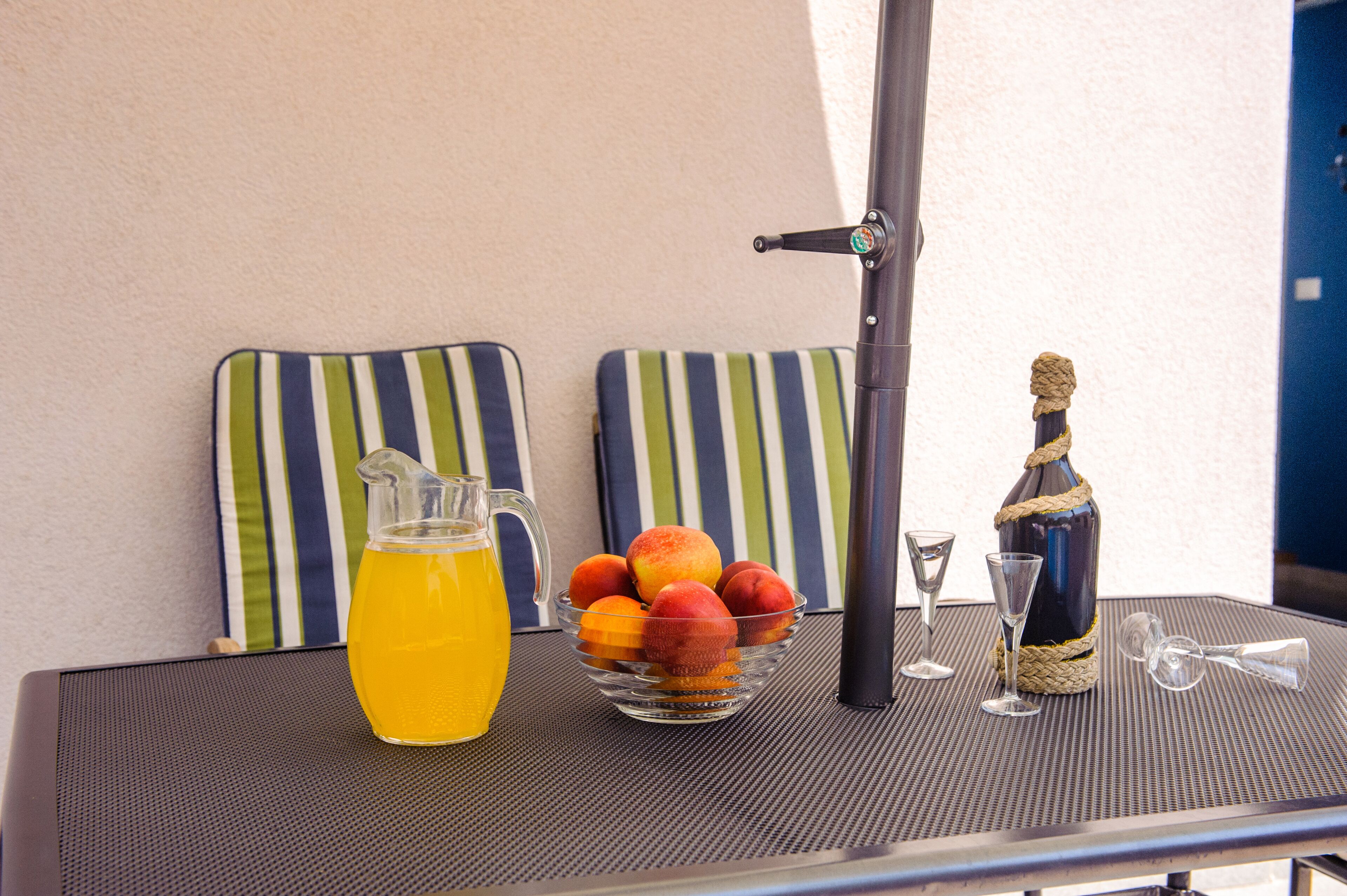 A table with a pitcher of orange juice, a bowl of fruit, a bottle of champagne, and two wine glasses.