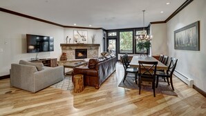 Uma sala de estar ampla com lareira, uma televisão grande e uma área de jantar com mesa e cadeiras de madeira.