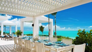 An outdoor dining area with white tables and chairs, overlooking a clear blue ocean.