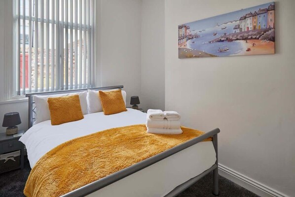 A hotel room with a bed, a painting of a coastal scene, and a window with blinds. - Host & Stay | Diamond One (Saltburn-by-the-Sea)