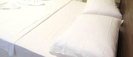A neatly made bed with white linens and pillows, a folded white towel, and a small table with a white cloth.