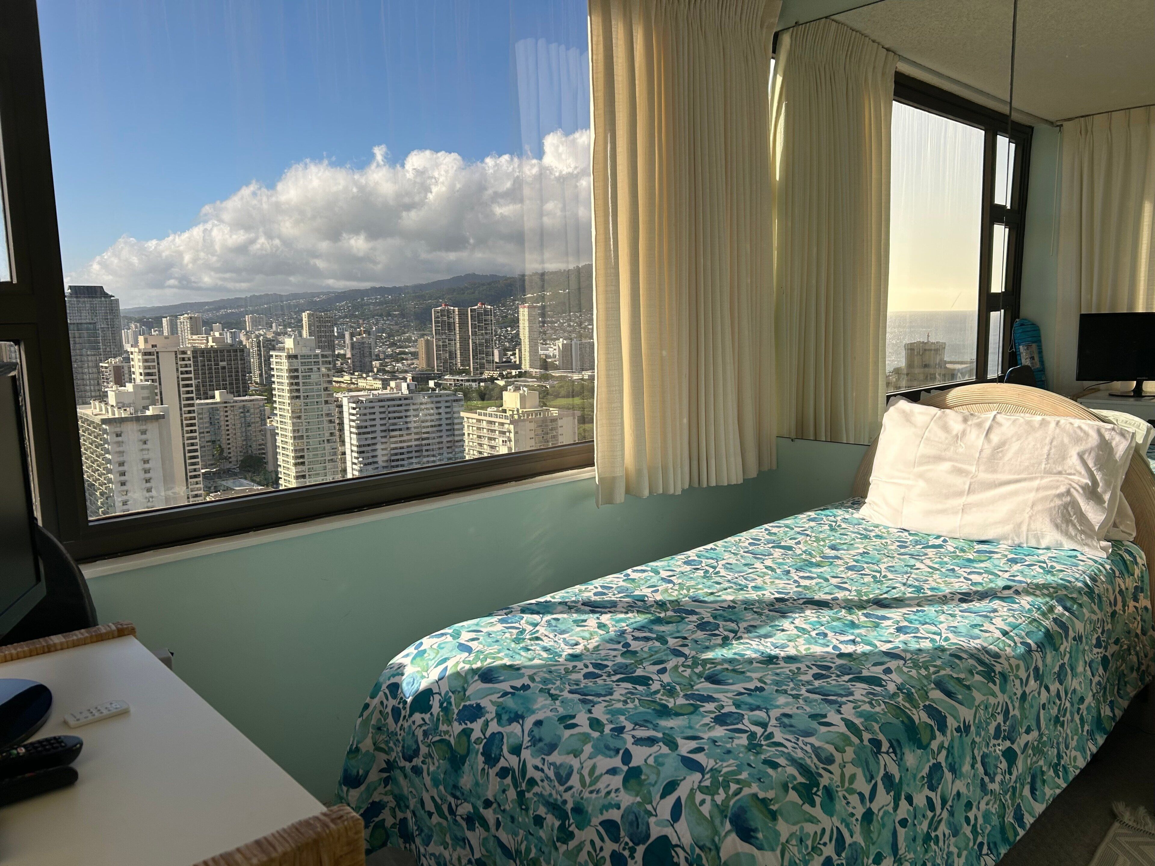 Une chambre d’hôtel équipée d’un lit, d’un bureau, d’une chaise, d’une télévision et d’une fenêtre donnant sur la ville.