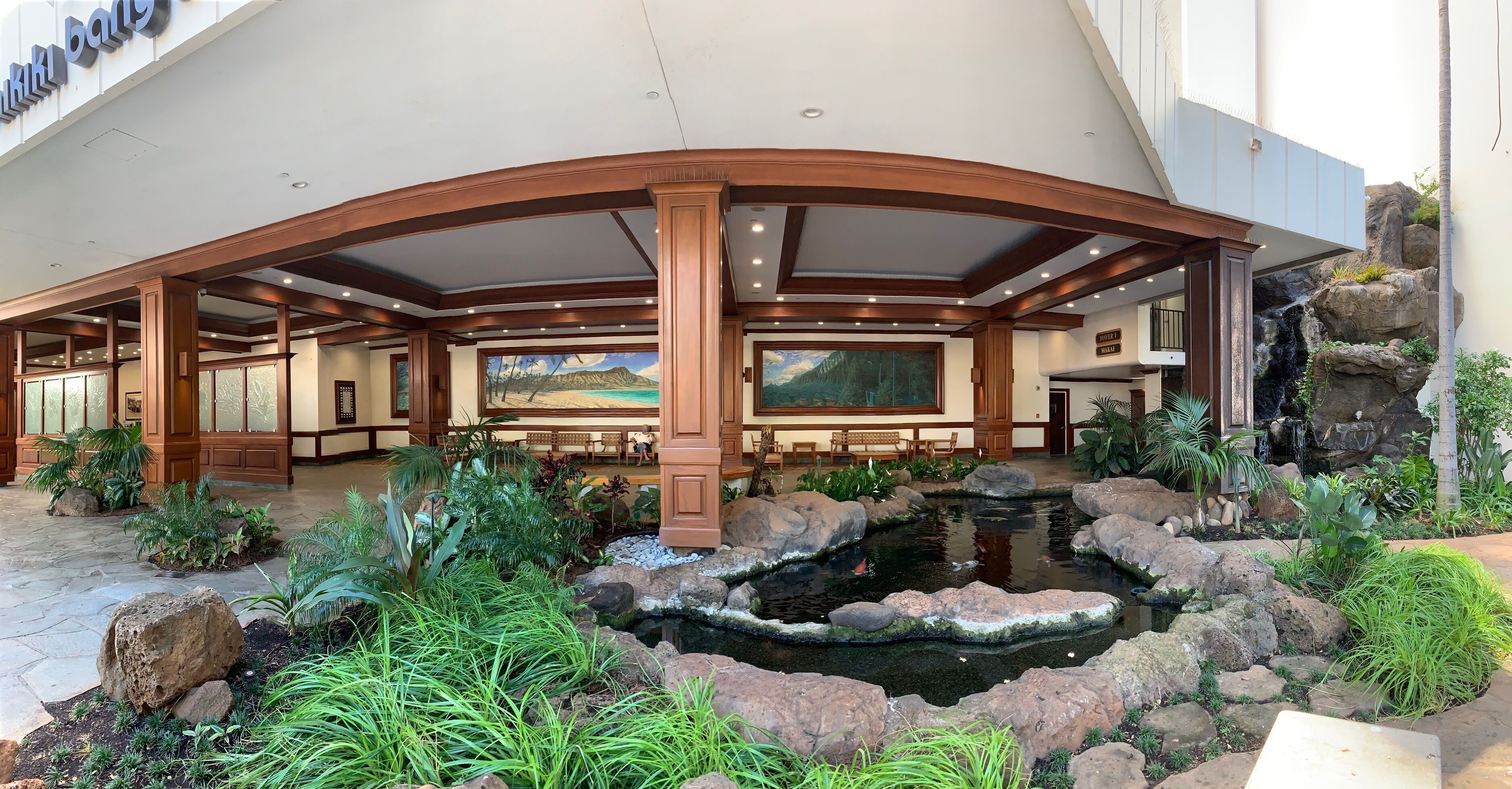 Un hall d’hôtel agrémenté d’une grande fresque murale, d’un bassin à carpes koï et d’une cascade.