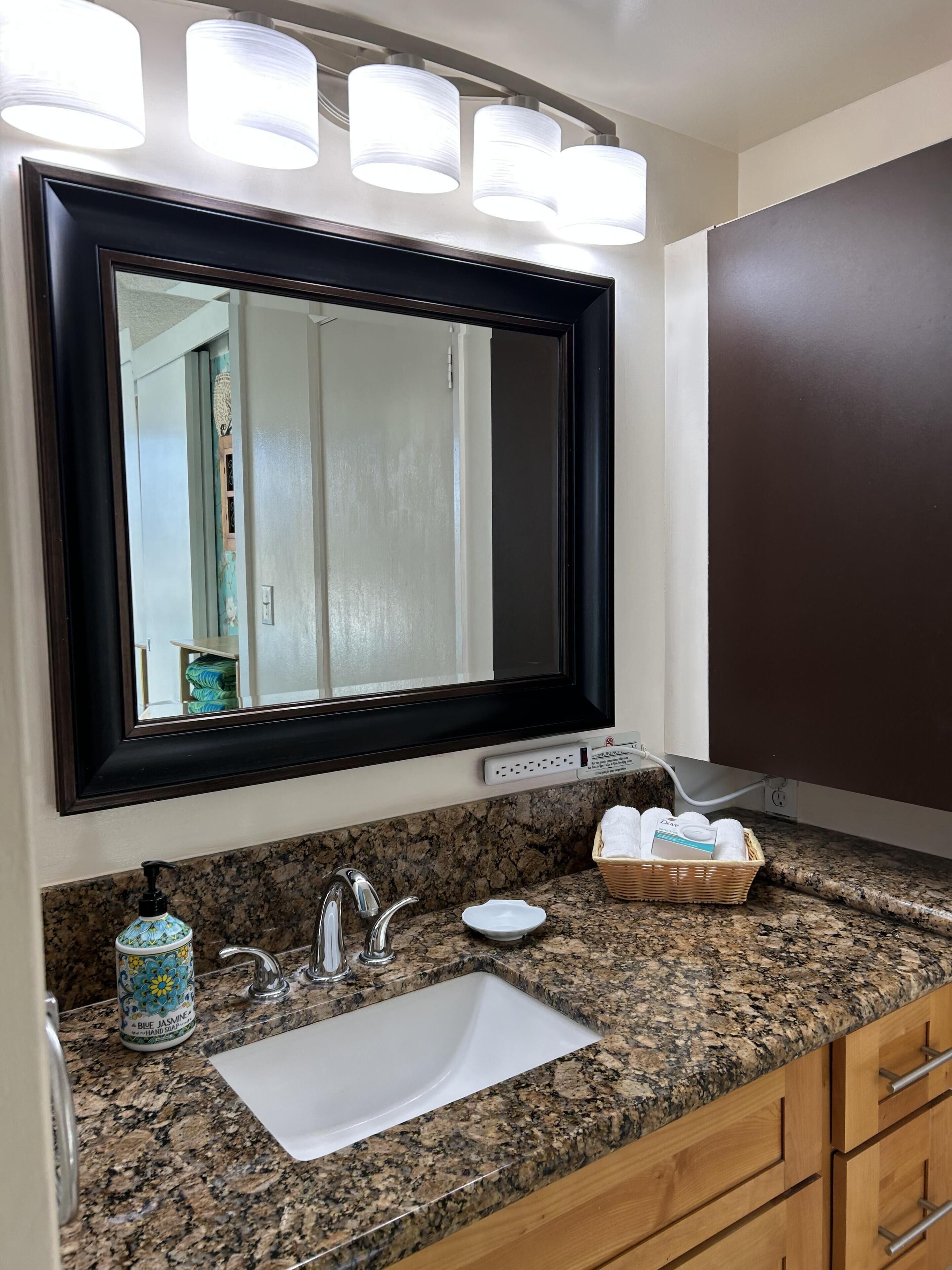 Bagno con lavabo, specchio e illuminazione a parete, con piano di lavoro in granito.