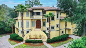 A yellow building with a central entrance, surrounded by palm trees and well-maintained gardens.