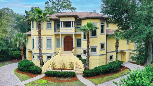 A yellow building with a central entrance, surrounded by palm trees and well-maintained gardens.