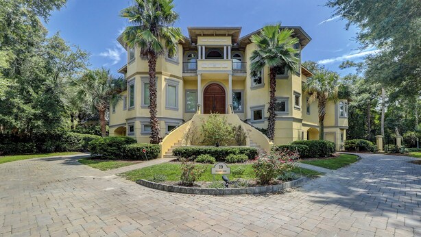 A multi-story building with a central entrance, surrounded by a landscaped garden with palm trees and shrubs.