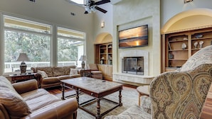 A spacious living room with leather sofas, a fireplace, and a large window overlooking greenery.