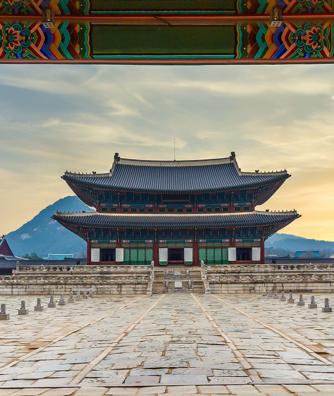 Ein traditionelles koreanisches Gebäude mit symmetrischer Gestaltung, das einen markanten Eingang und einen mit Steinen gepflasterten Innenhof aufweist.
