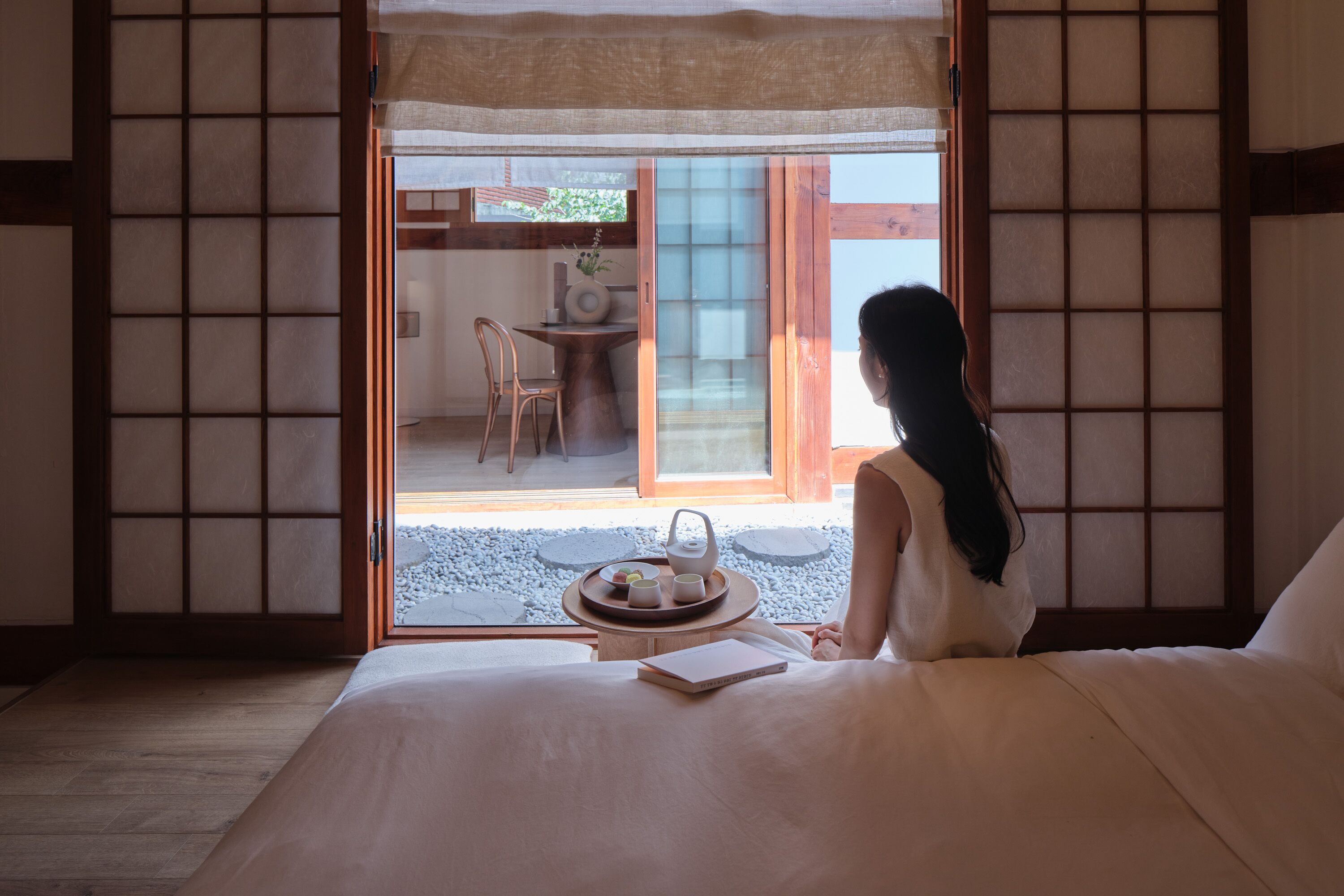 A room with a bed, a small table with a tray of food, and a view of an outdoor area with a table and chairs.